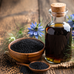 Schwarzkümmelöl in Glasflasche mit Schwarzkümmelsamen auf Holztisch, natürliche Darstellung