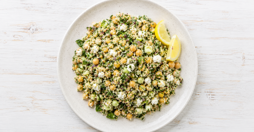 Quinoa-Salat mit Kichererbsen, Gurke, roten Zwiebeln, Kräutern, Feta und Zitronenspalten auf einem Teller