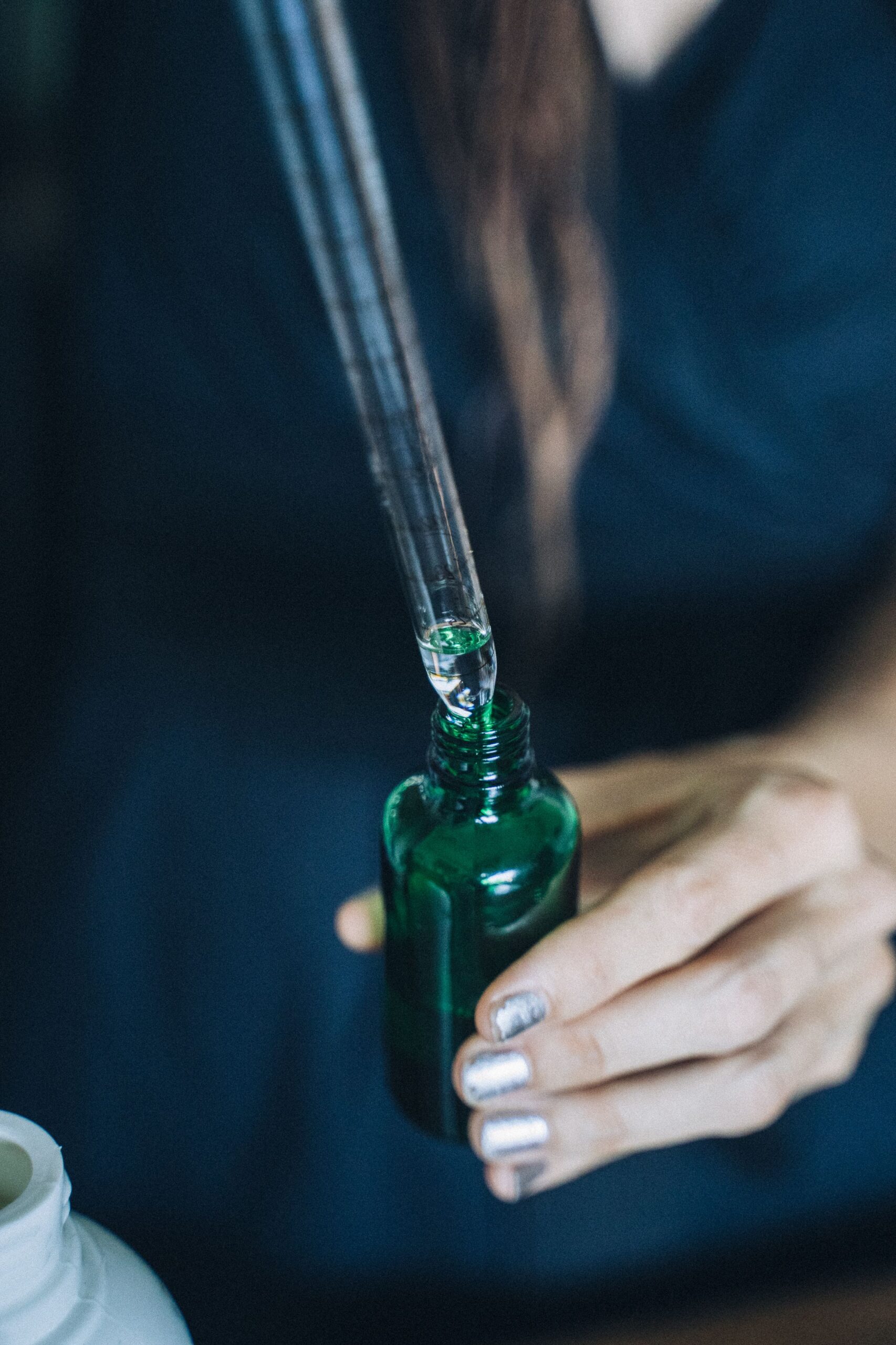 Frau hält eine Pipette mit Algenöl über einer grünen Glasflasche zur täglichen Omega-3-Ergänzung.