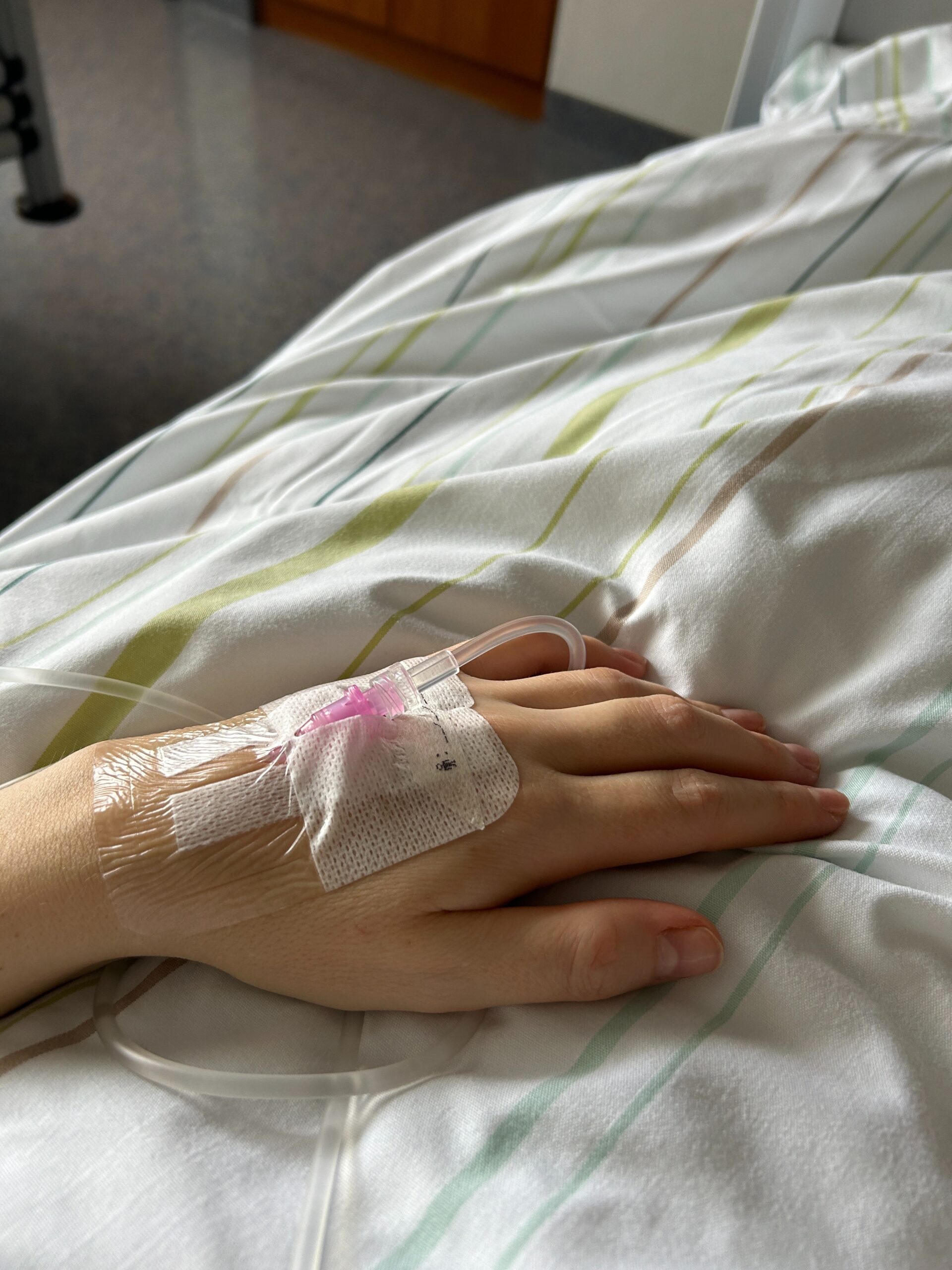 Hand mit venösem Zugang und Infusion auf einem Krankenhausbett kurz vor einer Mastektomie oder Brustoperation.